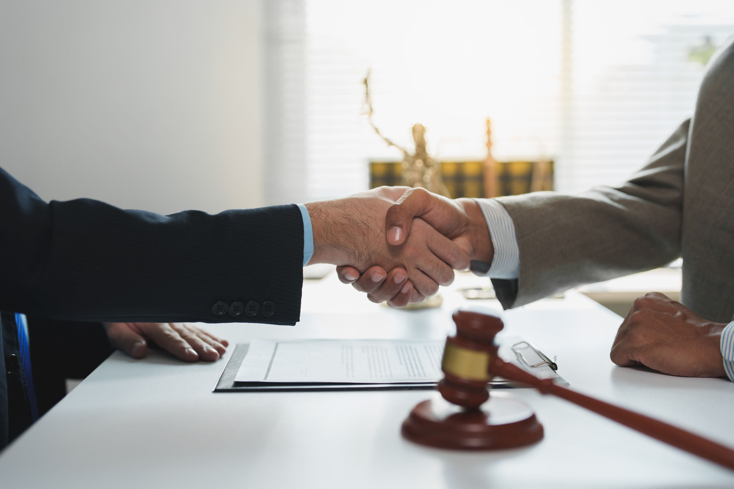 Two lawyers are shaking hands after successfully negotiating and signing a legal contract, symbolizing agreement and cooperation in a law office setting with a gavel on the table