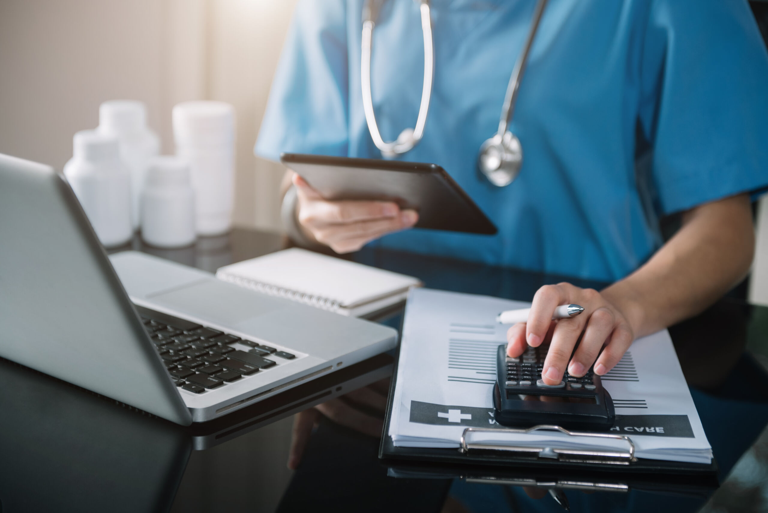 Doctor physician with tablet calculate medical fee costs & revenue. practitioner use calculator at Clinic.